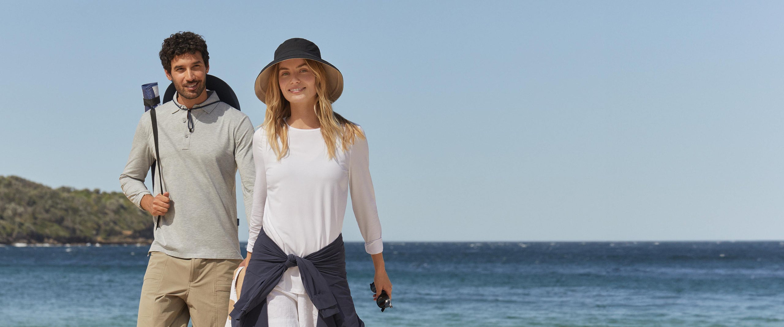 A man and a woman with the ocean behind them, wearing Solbari sun protective clothing.