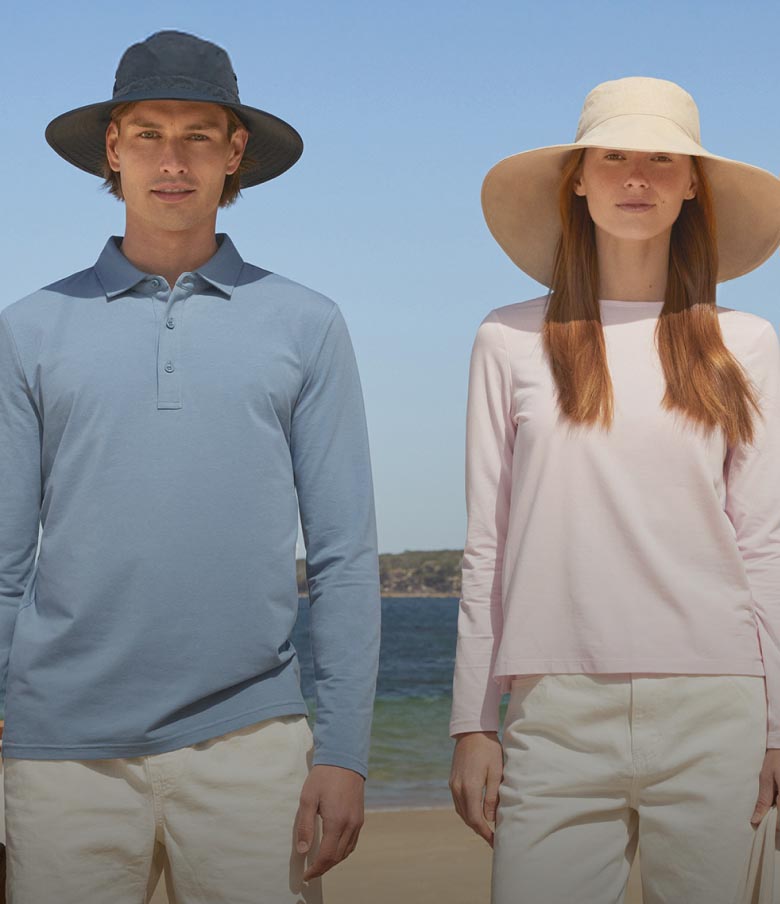A woman and a man wearing sun hats with the beach and sea behind them.