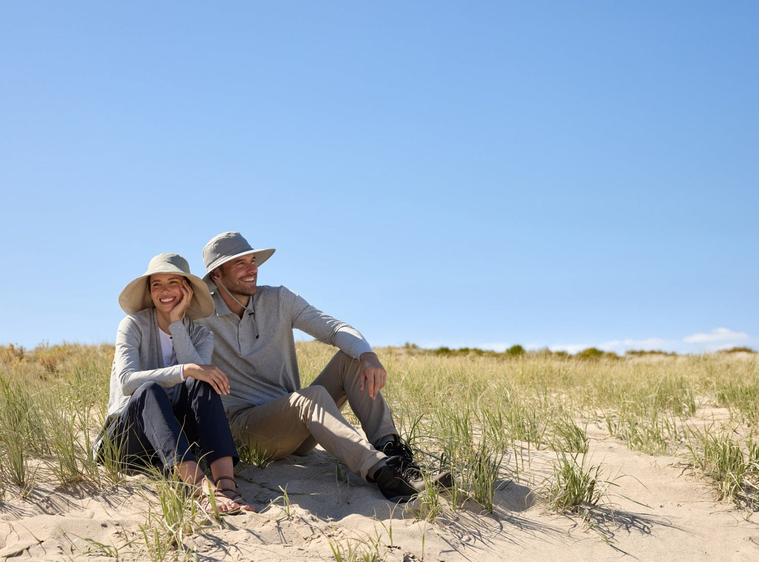 Couple wearing sun hats and UPF clothing on beach dunes