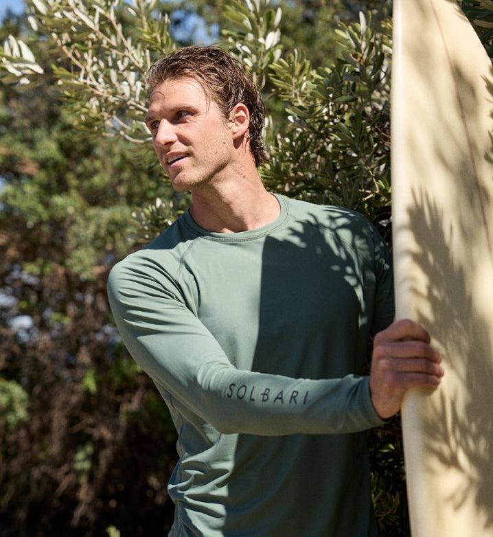 Man wearing a UPF 50 rash guard carrying a surf board.