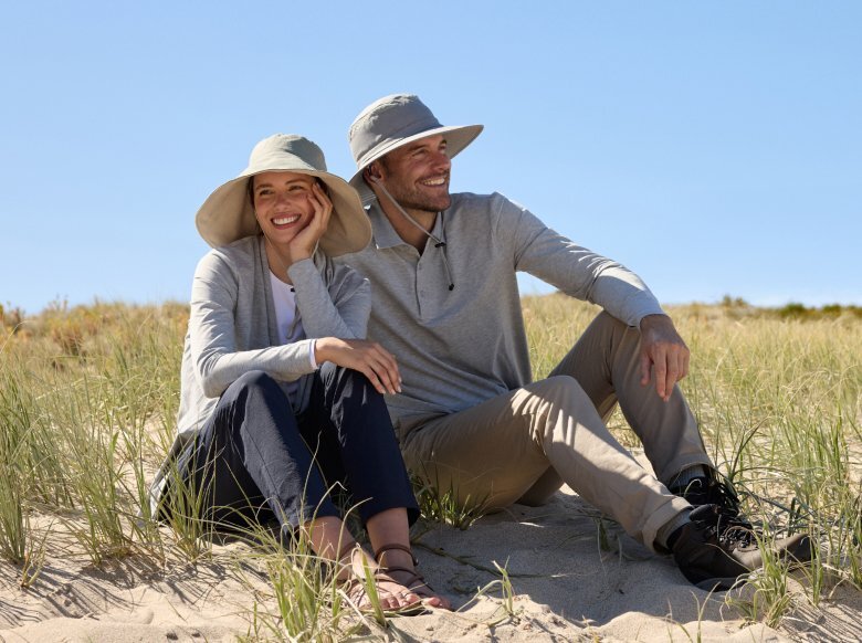 Couple sitting on the beach wearing Solbari sun hat and clothing.
