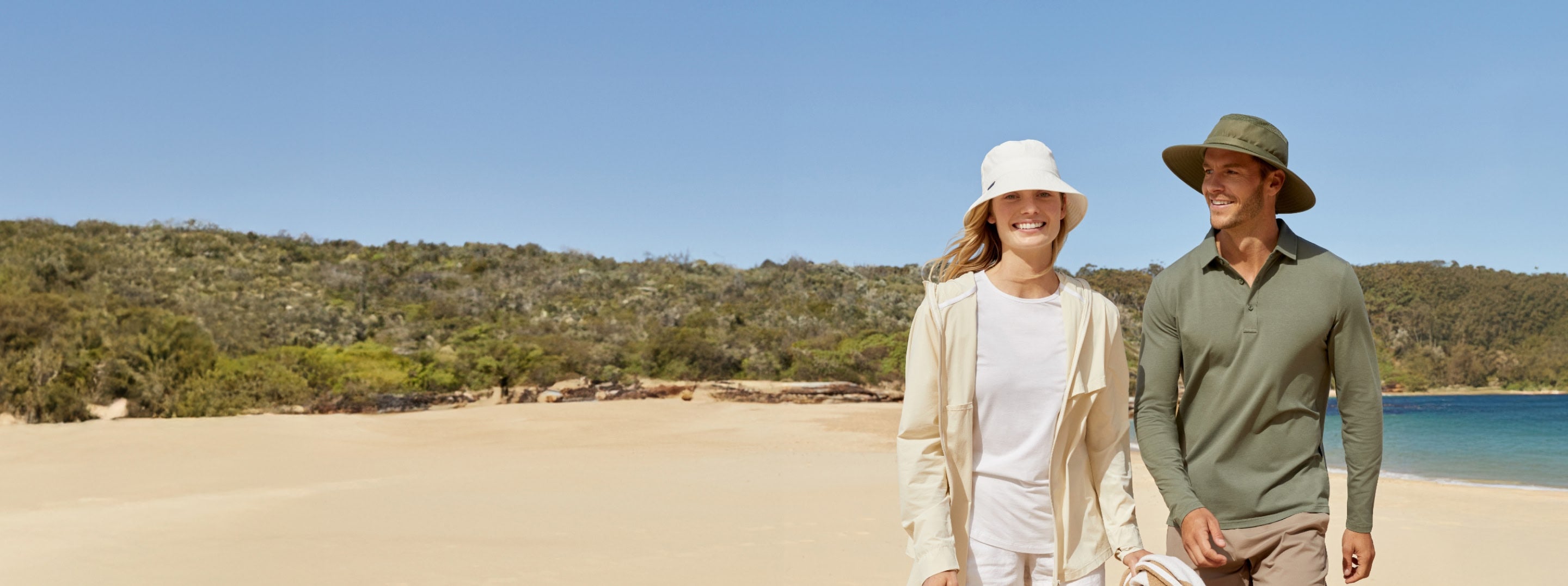 A man and a woman walking on a beach in Solbari UPF 50+ sun hats and clothing.