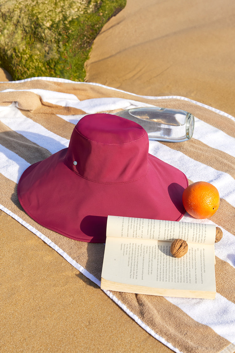 red_wide_brim_hat_placed_on_beach_towel