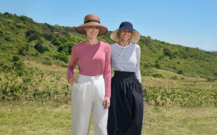 2_women_wearing_wide_brim_hats_against_green_hills