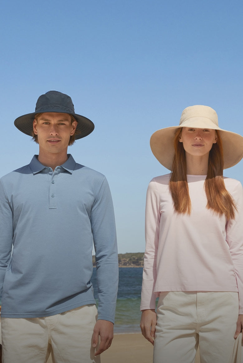 A woman and a man wearing solbari sun hats with a blue sky and the sea and beach behind them.
