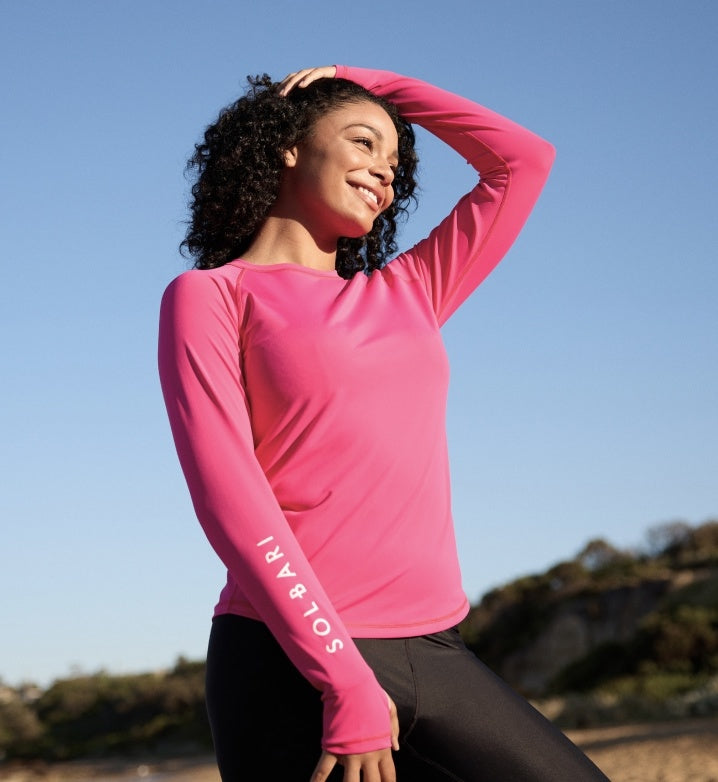 Woman in a pink Solbari rash guard advertising UPF 50+ swimwear.