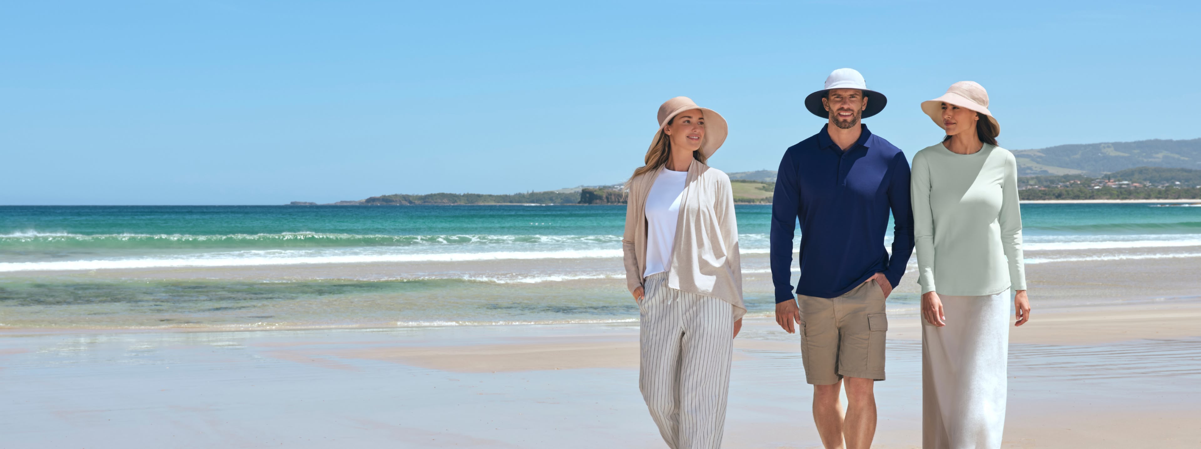 Three people walking on a beach wearing Solbari Sun hats and clothing.