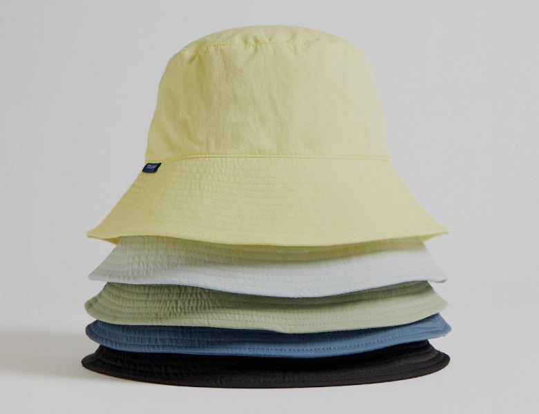 Bucket hats piled up in different colours on a light grey background.