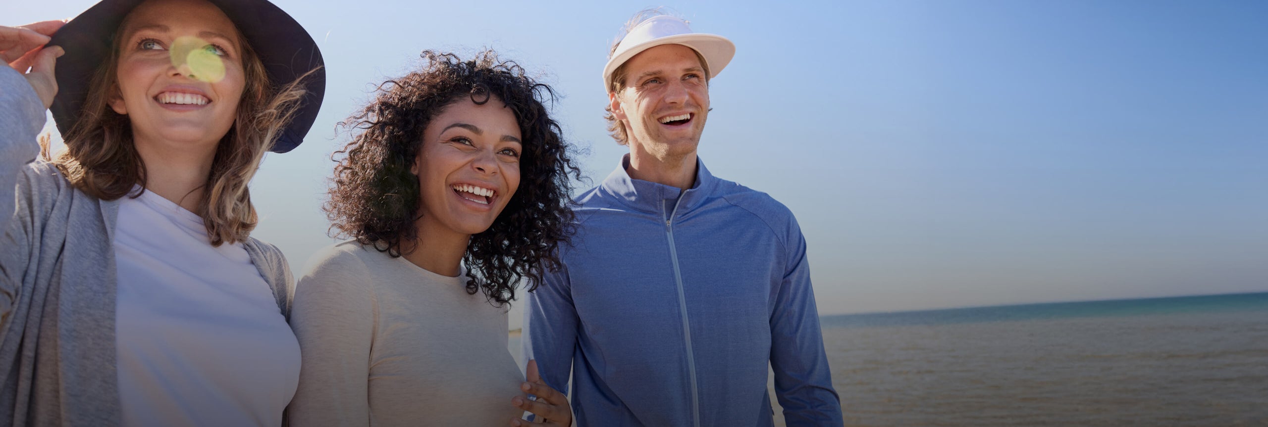 Two women and a man standing on the beach with the ocean behind them.