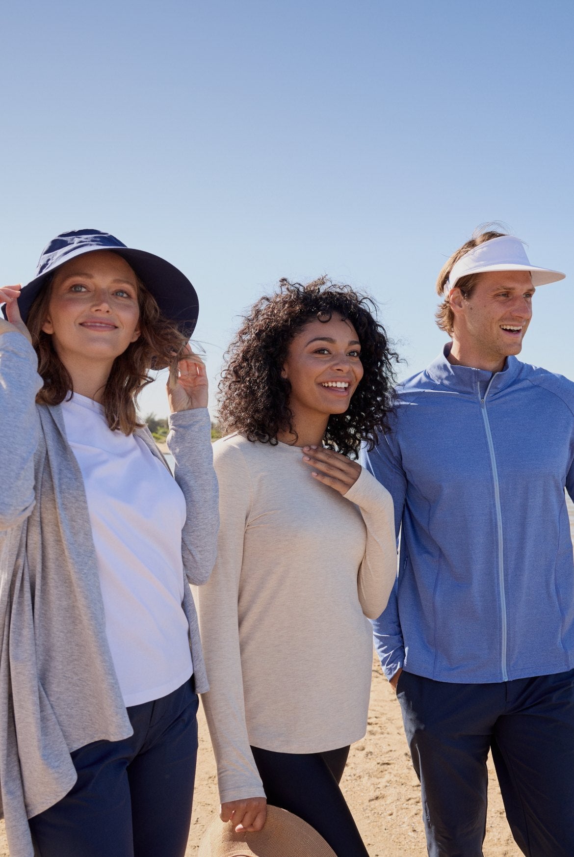 Three people standing on a beach in sun hats with blue sky in the background.