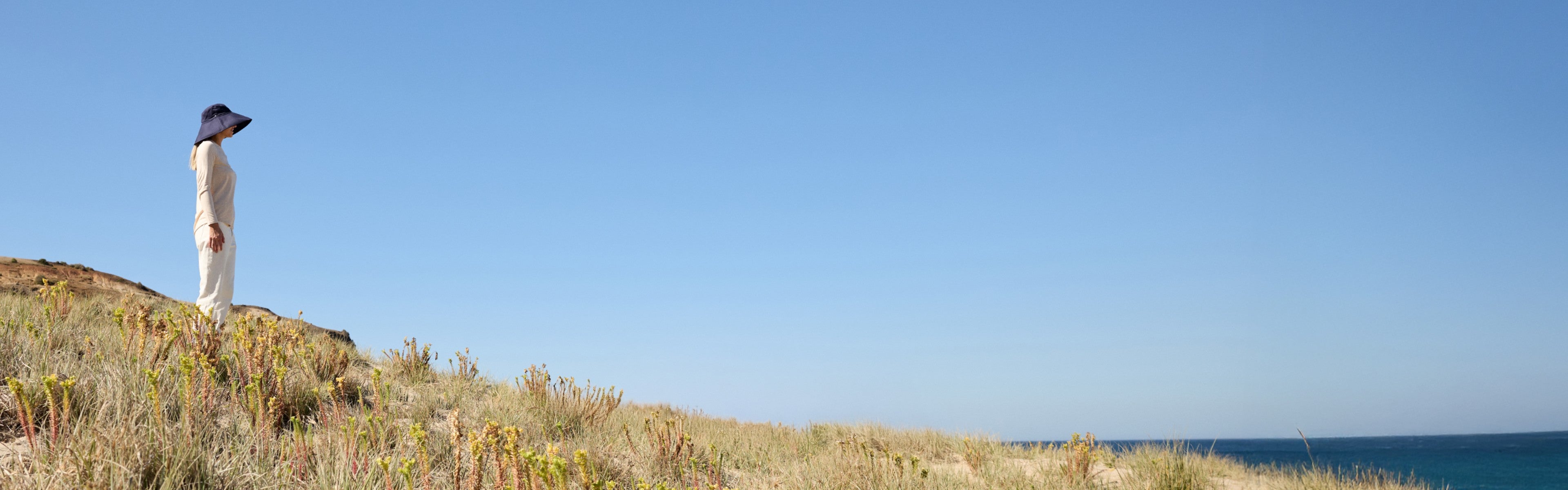 Woman walking near the sea in a Solbari sun hat and clothing
