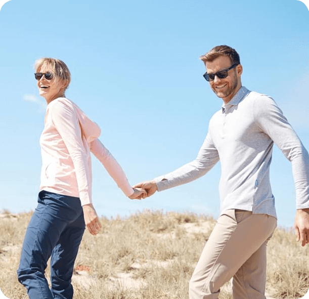 A man and woman holding hands walking on a hill with a blue sky in the background.