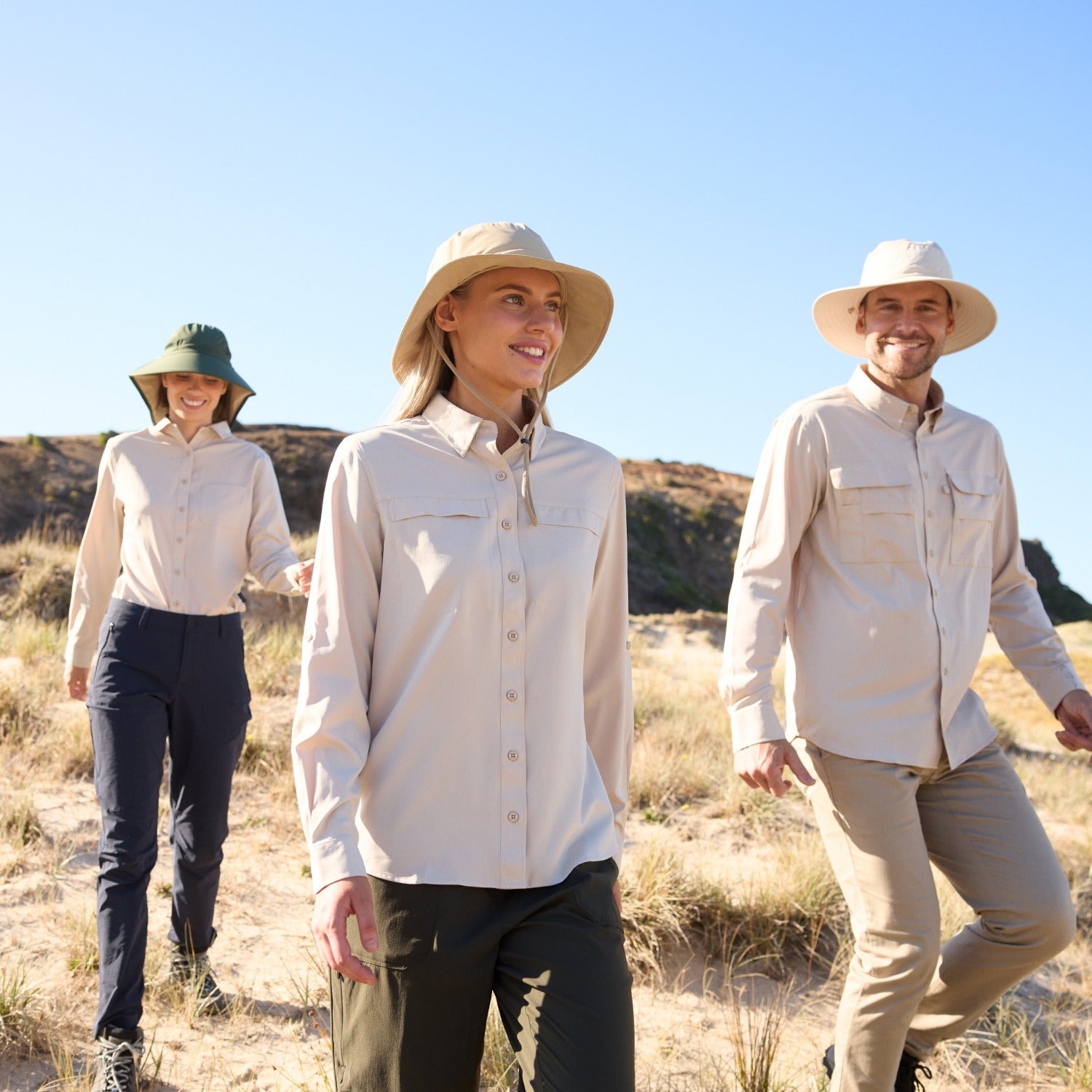 Three people walking in sun hats and beige shirts and trousers.